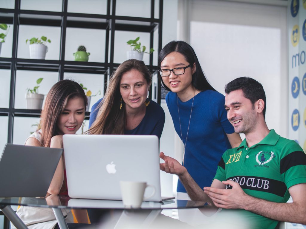 4 students from different countries huddling together around a laptop