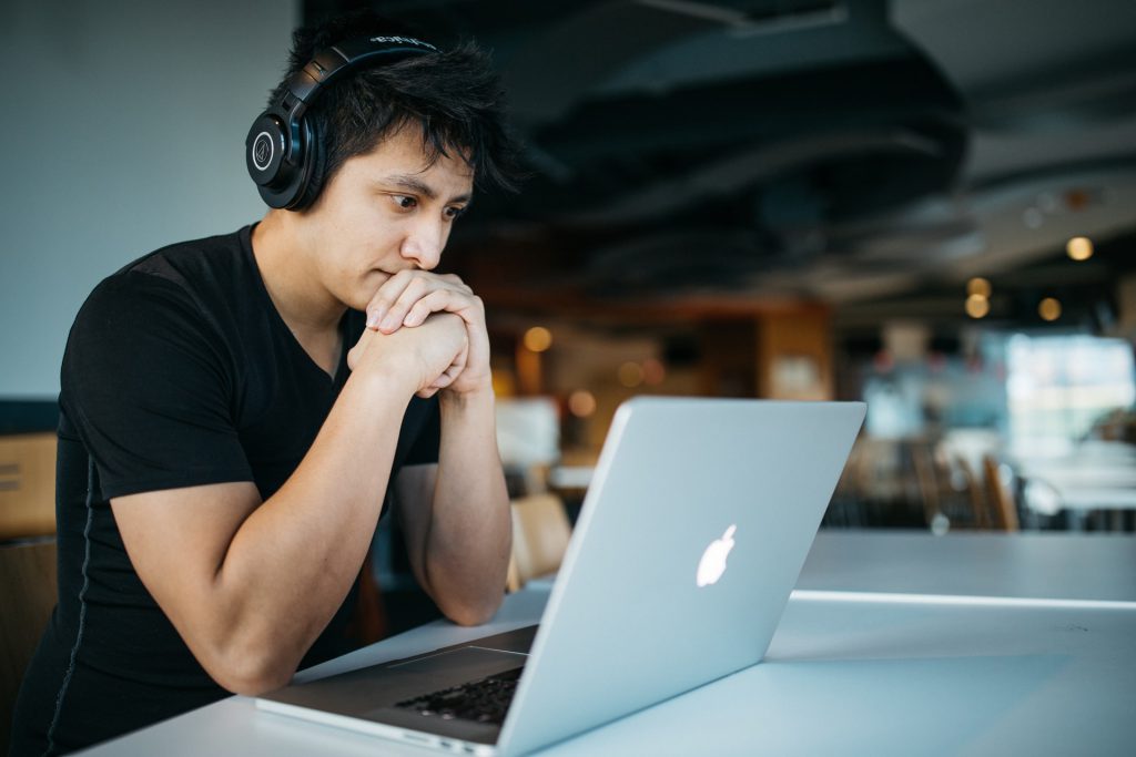 male student with headphones sitting down and looking at his laptop to study